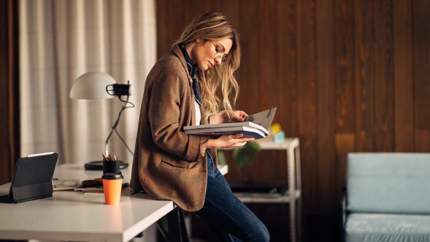 well dressed casual professional woman sits on her desk while reading a report in a modern office