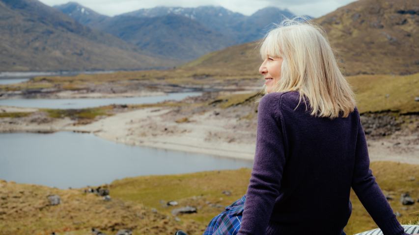 mature woman sitting in nature and enjoying the view of a lake and mountains