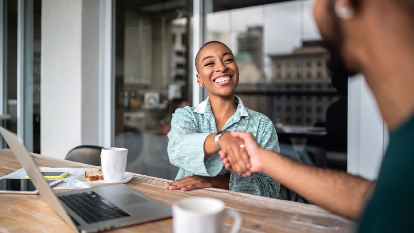 woman in a pinstriped shirt is shaking hands with a man during an informal business meeting on a patio