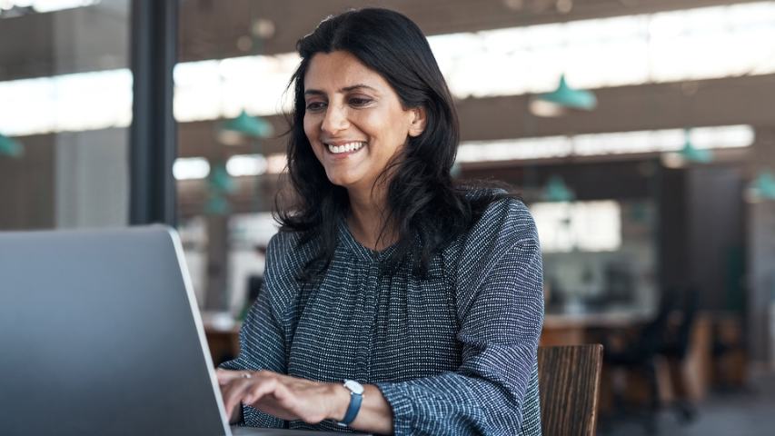 professional woman smiling while typing on a laptop at her desk in an office