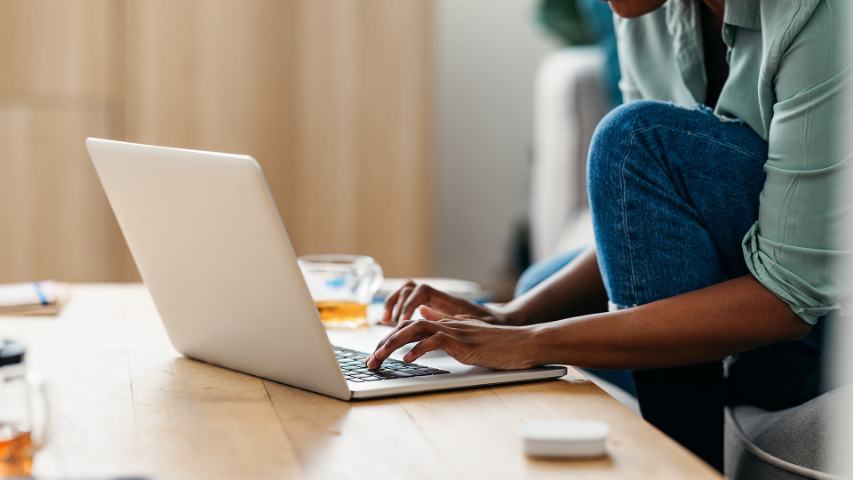 close up of casually dressed woman using her laptop at home on a pine table