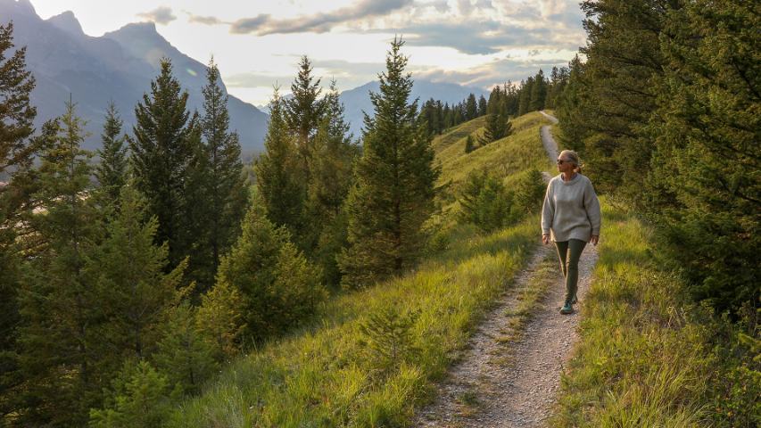 mature woman walks on a path through the countryside in the late afternoon