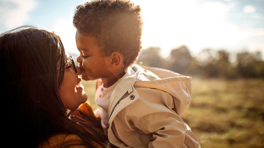 a young boy kissing his mother on the nose while they're outside
