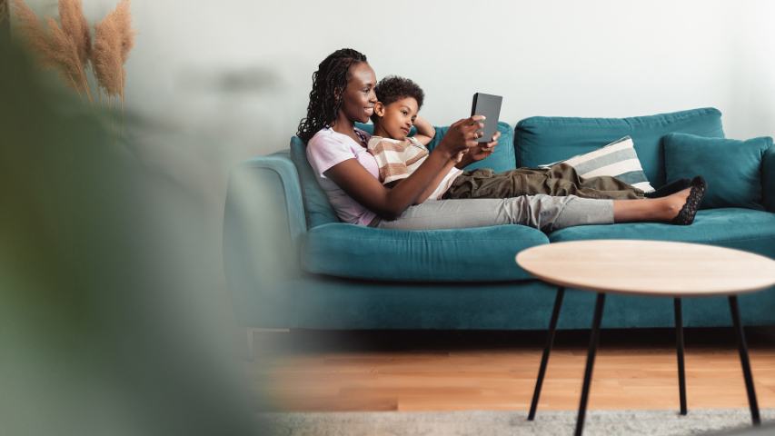a mother and her son are lying on a sofa and looking at a tablet