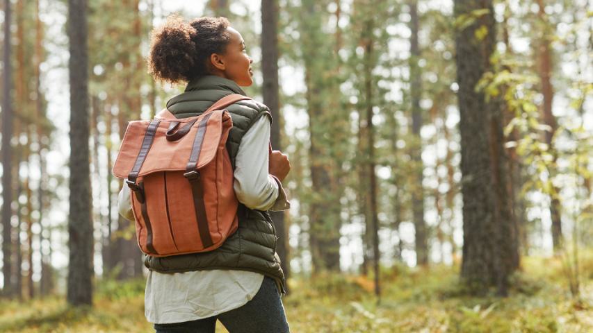 woman with a backpack walking through a forest in the sunlight