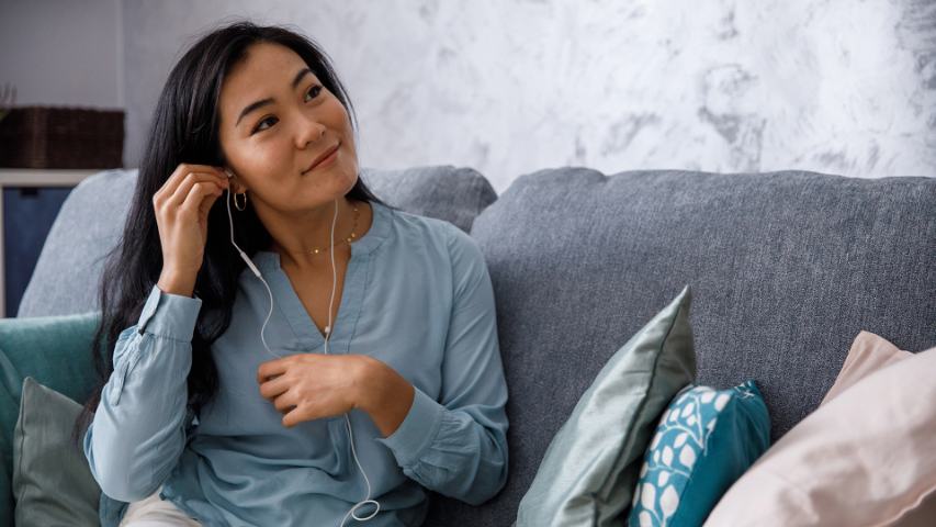 happy relaxed woman adjusting her earbuds while sitting on a blue sofa