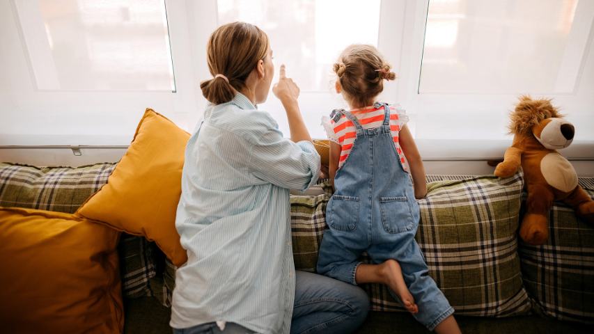 mother and child sit on a sofa while the mother points out something through the window