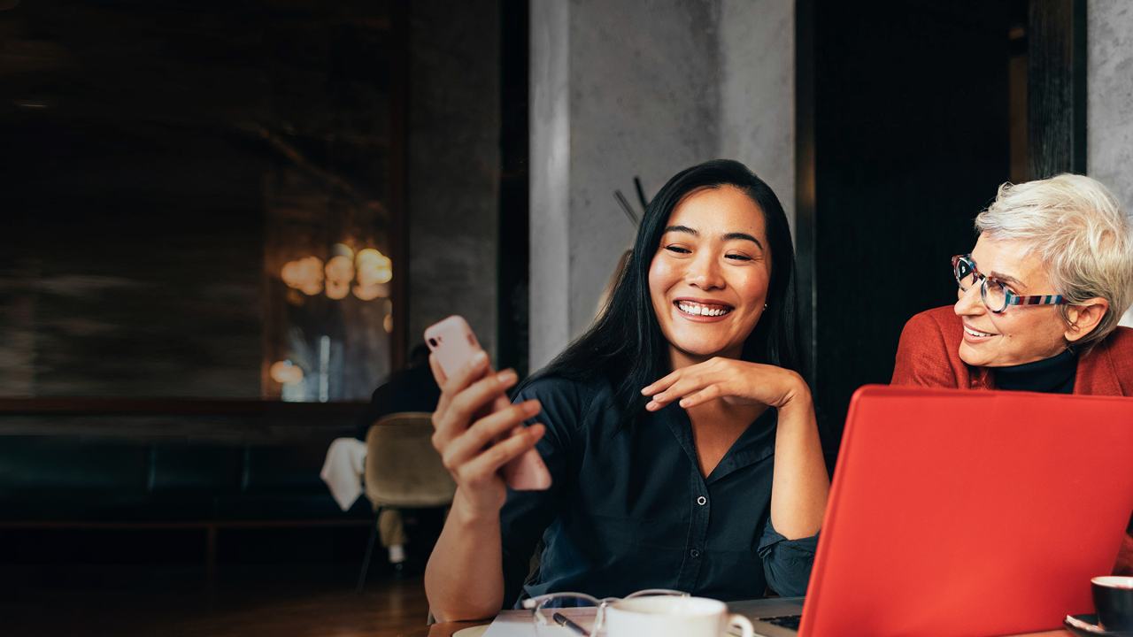 Business people having a casual business meeting in restaurant. Young woman showing document on her mobile phone to her colleagues