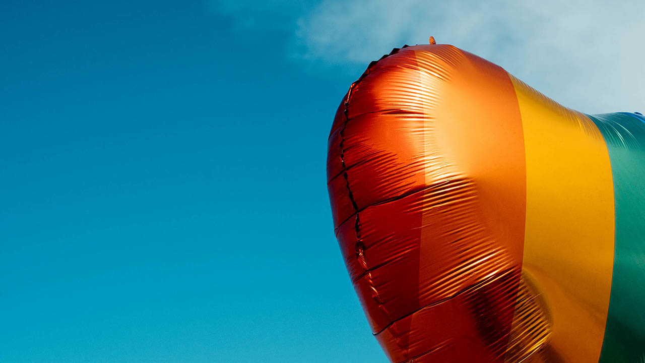 A heart shaped rainbow balloon being held in the sky