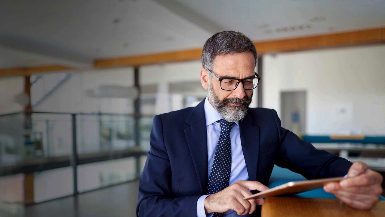 a professional man in suit and tie is concentrating on his tablet while standing in an office lobby