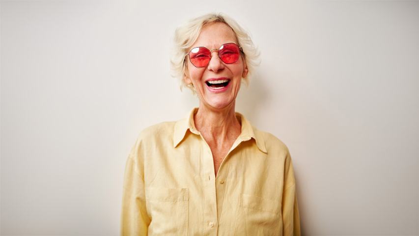 laughing elderly woman in a yellow shirt and red glasses