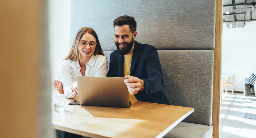 male and female professionals siting in a booth in their office on a conference call with a laptop