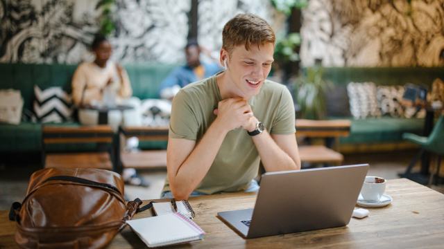young man using his laptop with earbuds at a cafe 