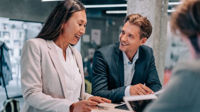 a phappy rofessional woman is chatting with her male coworker whle a third woman looks on