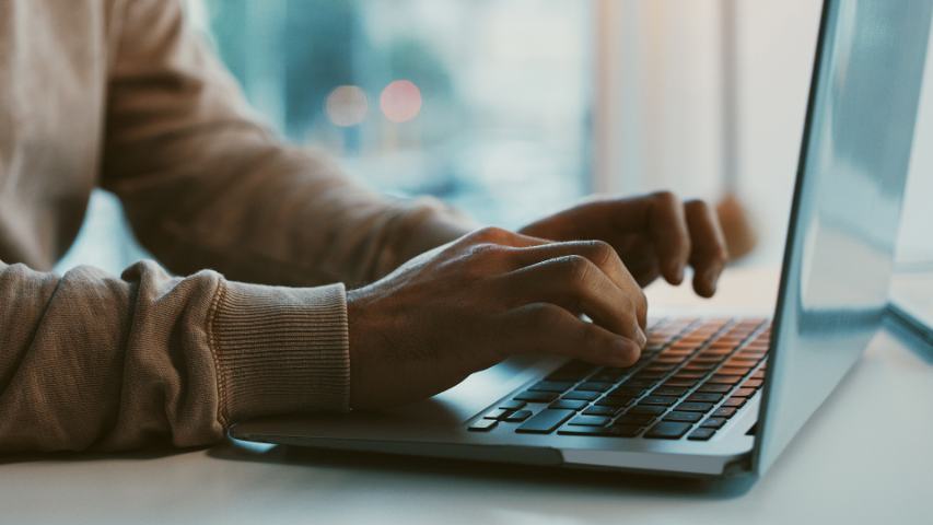 close up of a man's hands on a laptop keyboard with an out of focus view behind