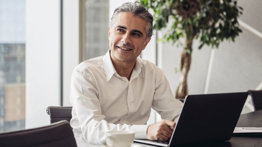 man in an office pauses during typing at his laptop to think 