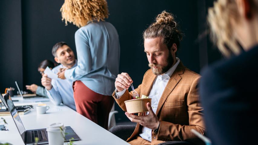 man in a busy modern offfice eating a salad at his desk