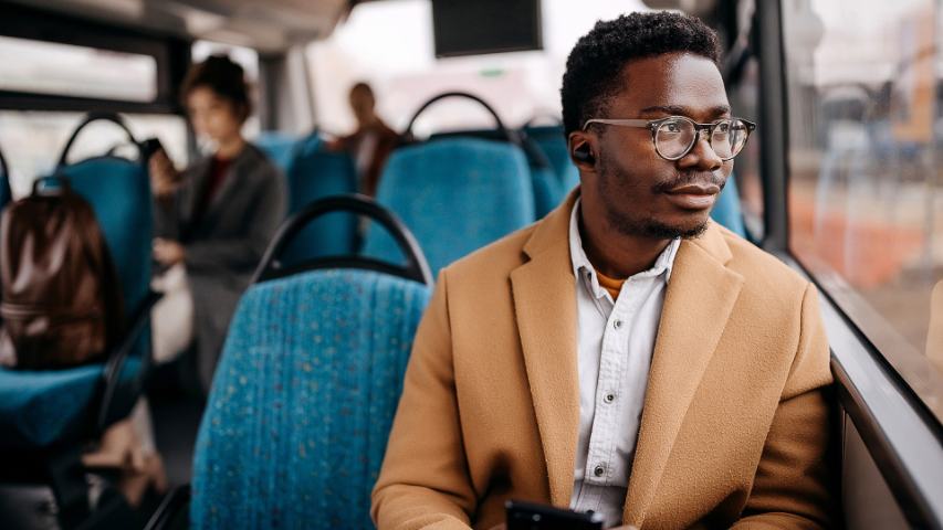 man in a camel coat and glasses looking out the window while on a bus