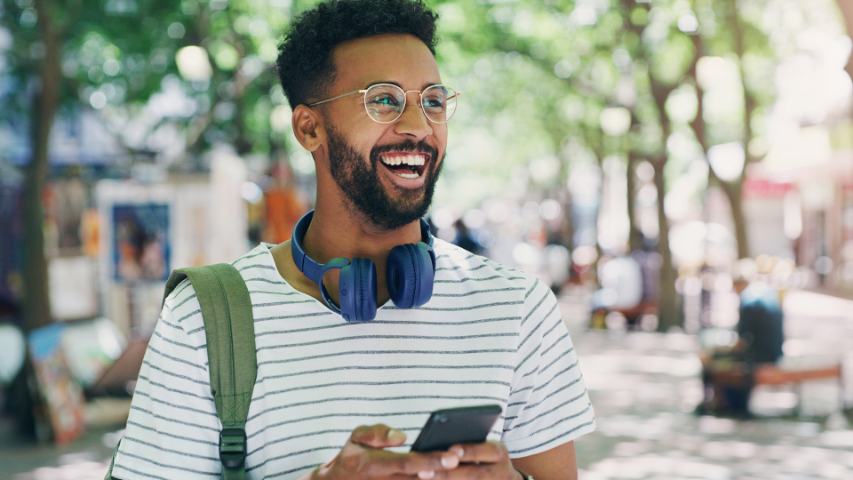 man with glasses and blue headphones is laughing while using his phone outside