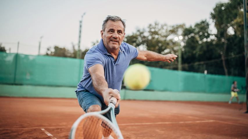 mature man in a blue polo shirt playing tennis on a clay court