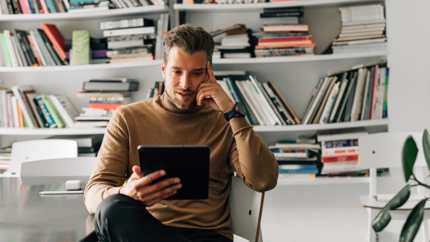 Male sitting in front of office bookshelves looking at tablet screen