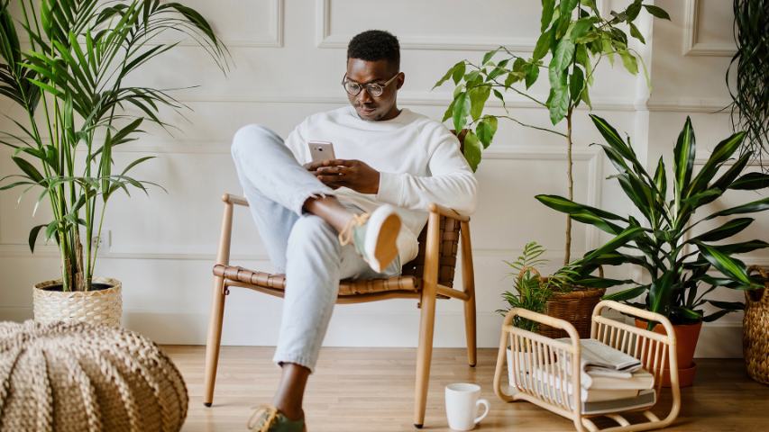 serious man using his phone while seated in a stylishly decorated home with plants