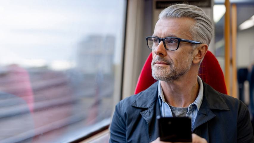 A man uses his phone and looks wistfully out the window while on a train