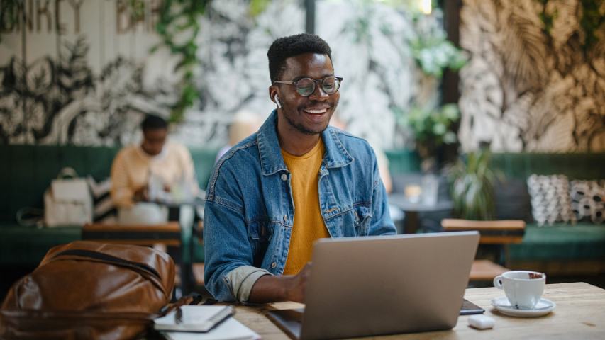 Smiling male working on laptop in coffee shop