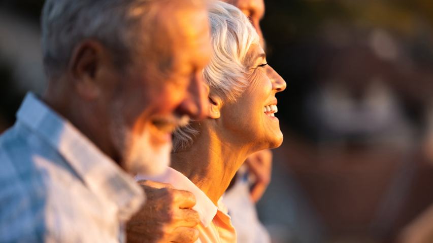 mature smiling woman being embraced on each side by mature men as they stand in golden light