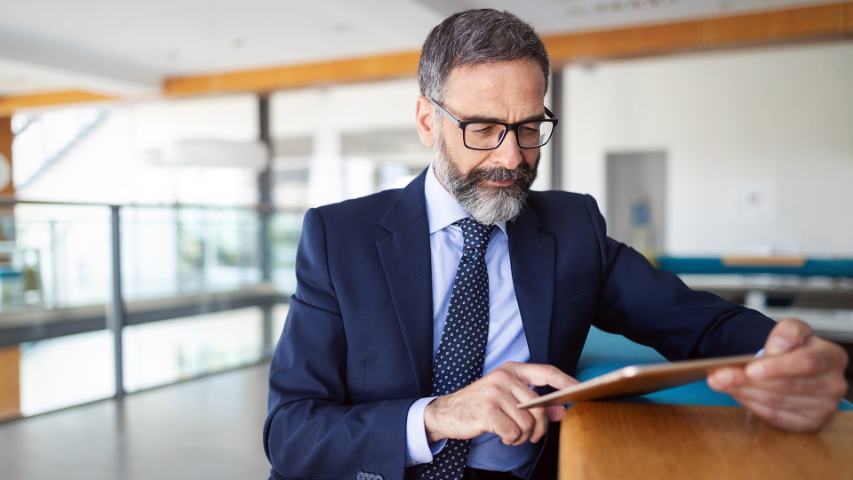 a professional man in suit and tie is concentrating on his tablet while standing in an office lobby