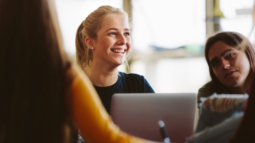 a happy woman is enjoying working at a laptop with her two female colleagues