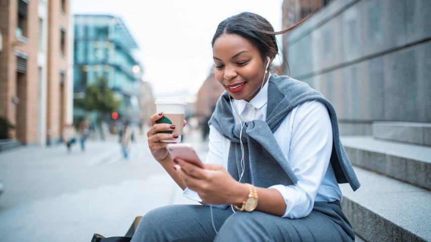 professional woman using her phone with earbuds while sitting outside with a coffee