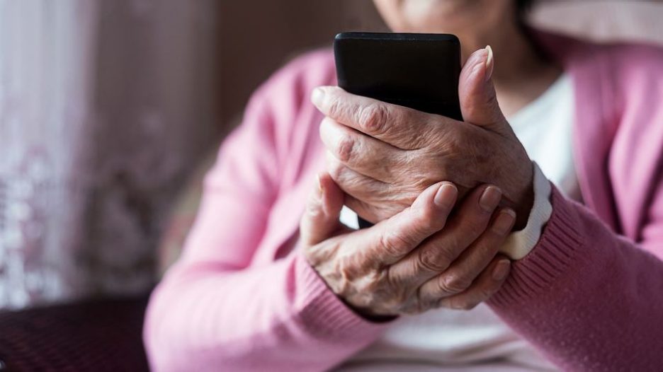 close up of a senior woman in a pink cardigan holding a mobile phone