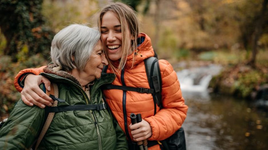 Senior woman and her granddaughter hiking on mountain, walking through forest