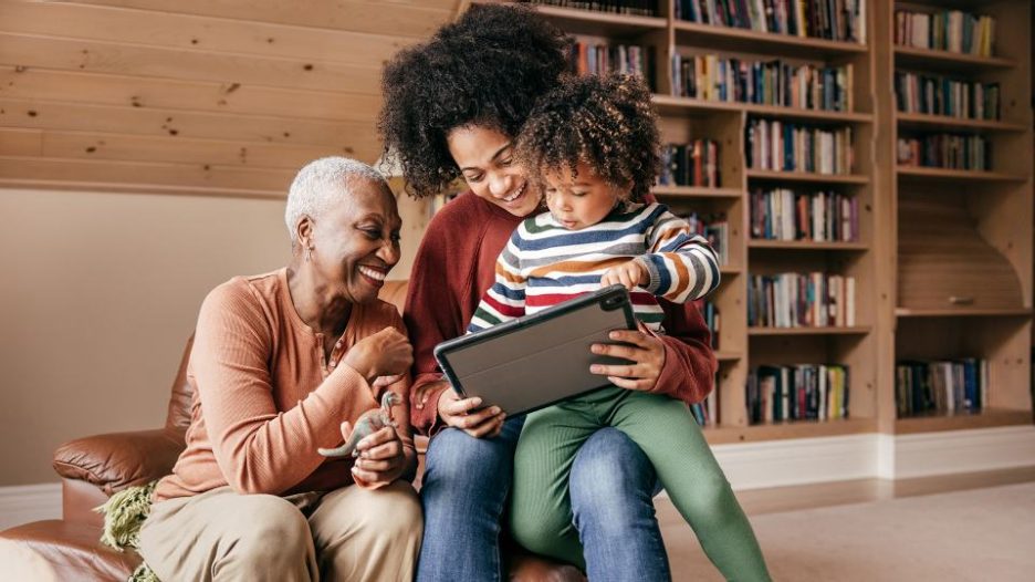 A happy man holding an uncertain toddler while a smiling woman looks on