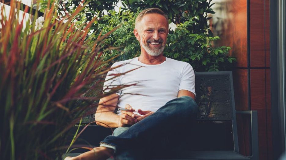 Smiling male sitting in balcony or garden area with lots of plants