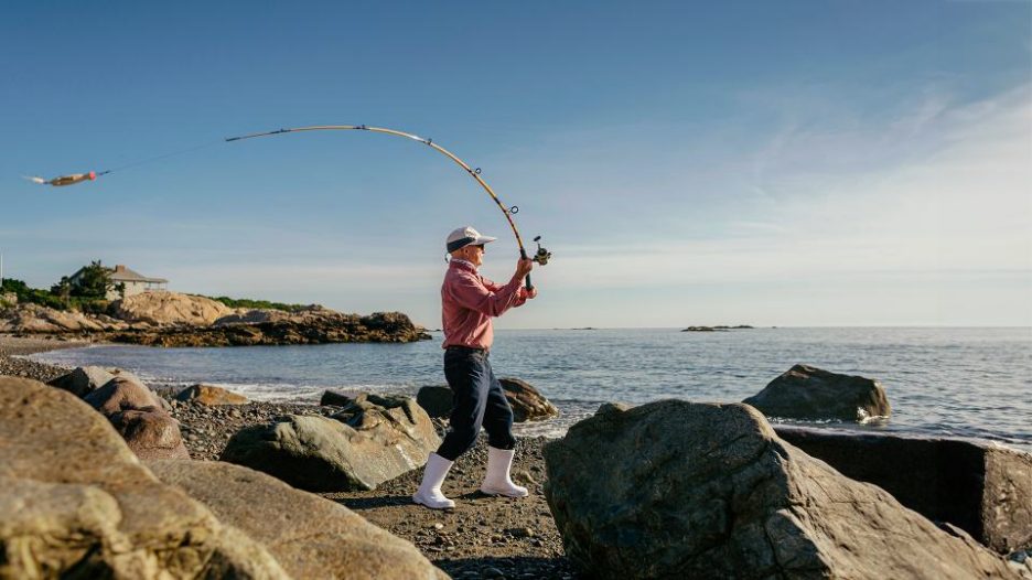 elderly man casting his fishing rod on a rocky beach.
