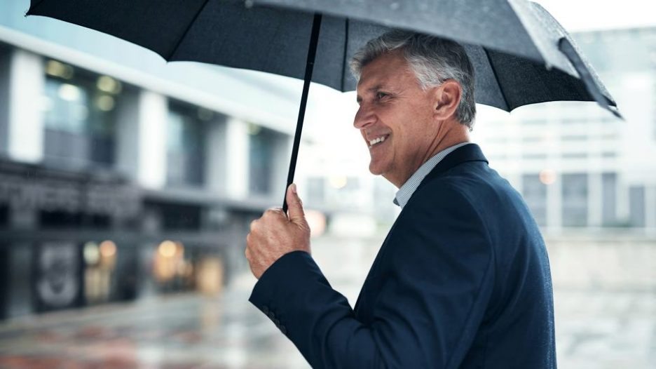 a man in suit and tie is happy while outside in the rain because he is protected by his umbrella
