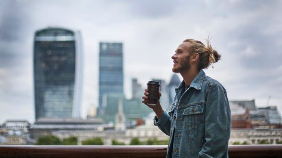happy man in a denim jacket enjoys coffee while walking through the city