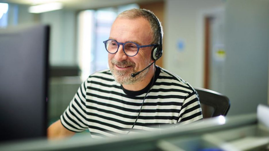 Smiling man with headset looking at computer screen in call centre