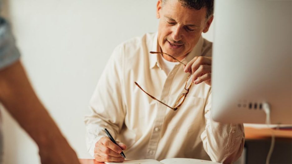 Smiling man with headset looking at computer screen in call centre