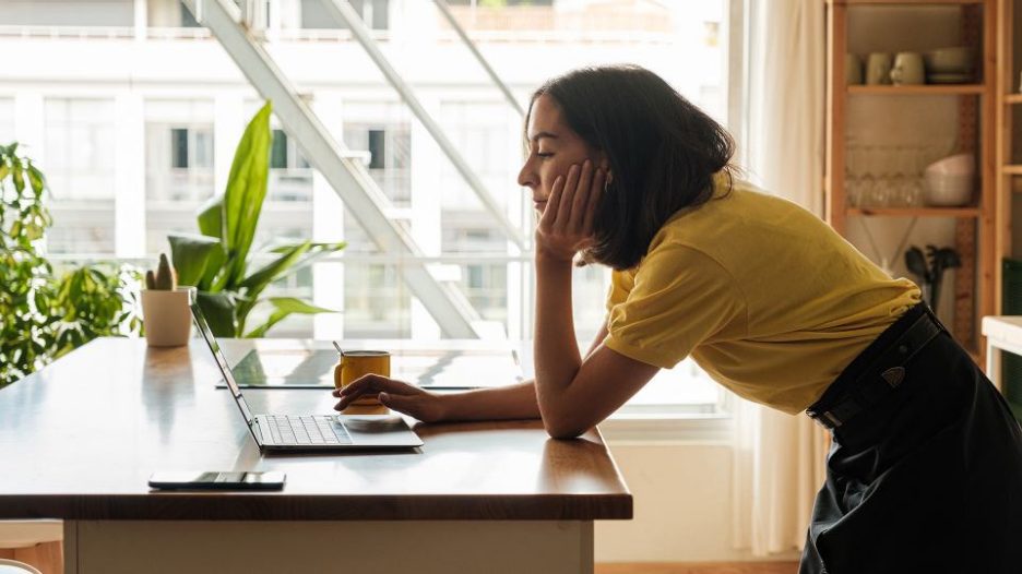 smiling woman working from home on her laptop is being helped by her dog