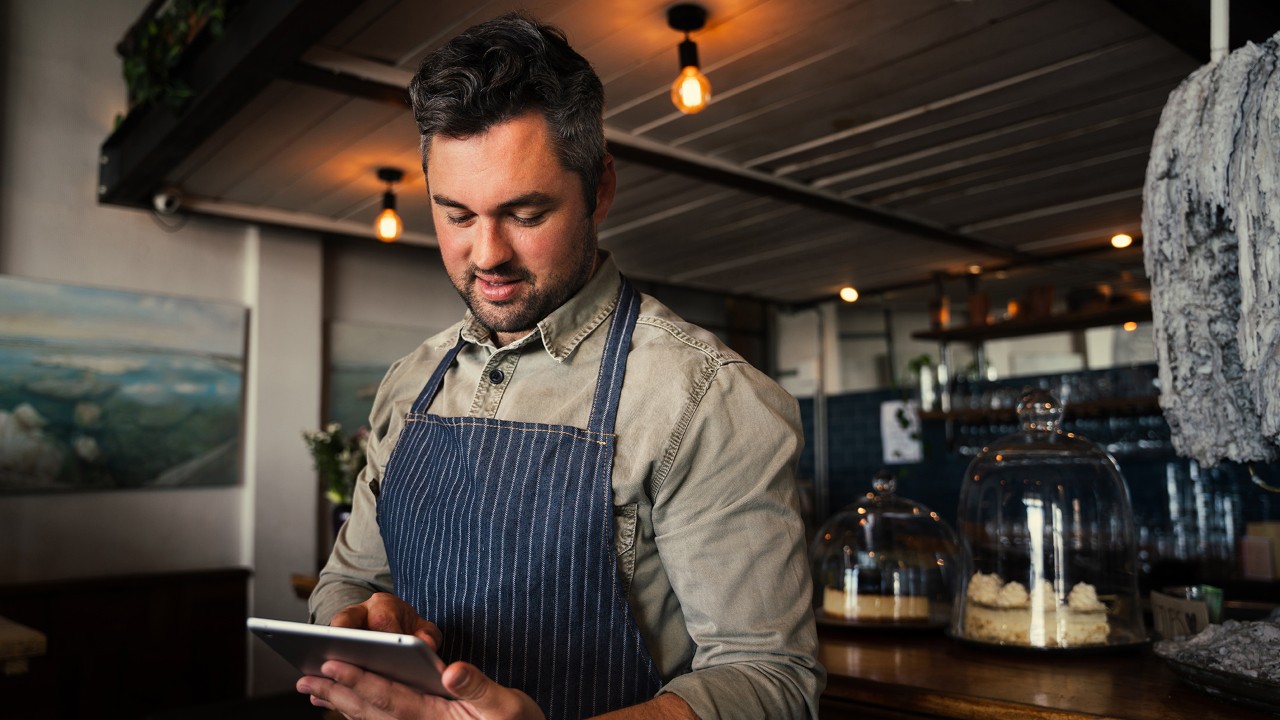 Male wearing apron in restaurant bar area looking at tablet Male wearing apron in restaurant bar area looking at tablet
