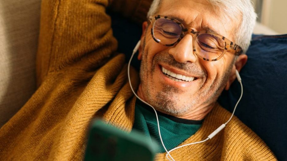 elderly man laying on couch and using his mobile phone with headphones