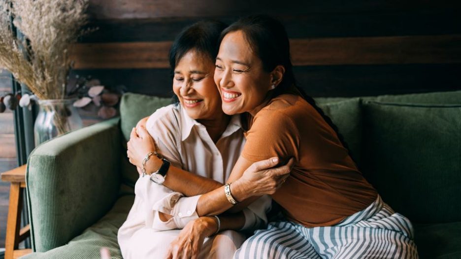 happy woman hugging her mother as they sit on a green sofa