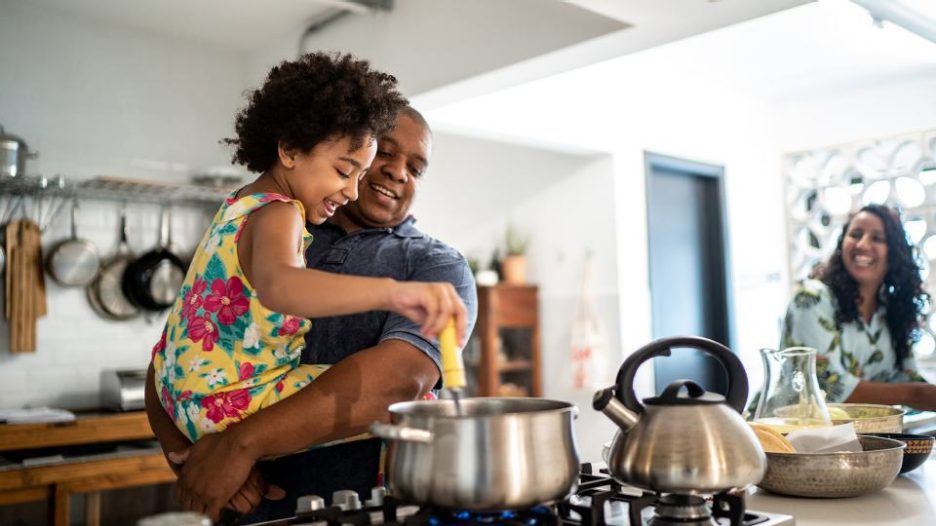 a father shows his yound daughter how to cook while the mother looks on