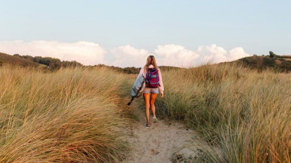 back view of woman walking on sandy path by grassy seashore