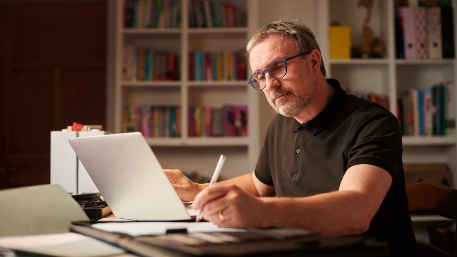 man at home on his laptop writing notes