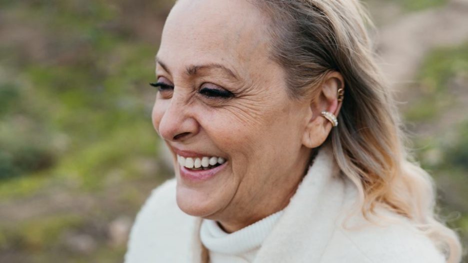 Portrait of a senior woman in a white jumper smiling while in a field
