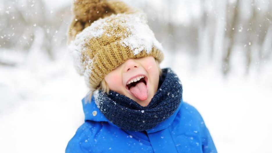 young child in a beanie and scarf tasting the snow